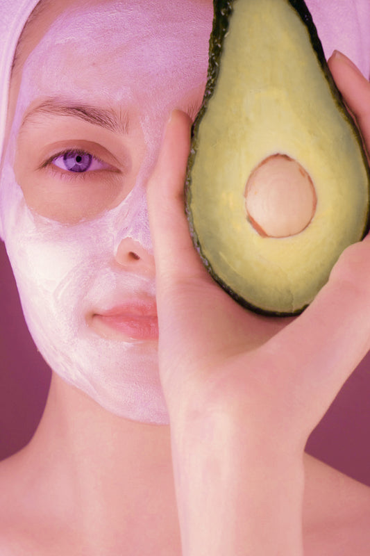 Woman doing facial mask SPA holding half avocado with hand, covering left eye