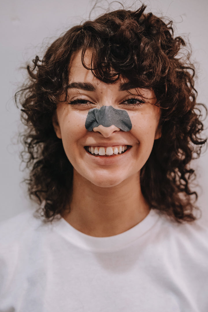 smiling woman with strip facial mask for blackheads on nose