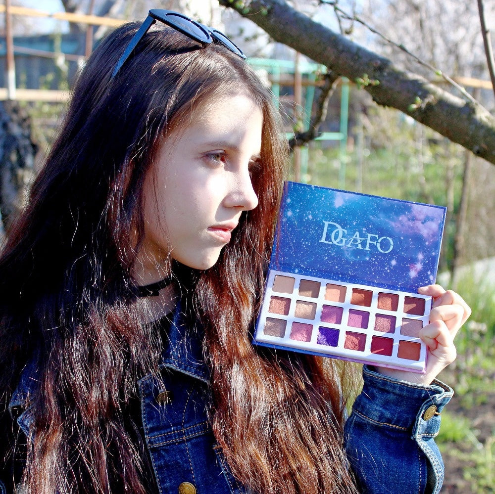 A young lady holding an open pigmented eyeshadow palette under sunshine